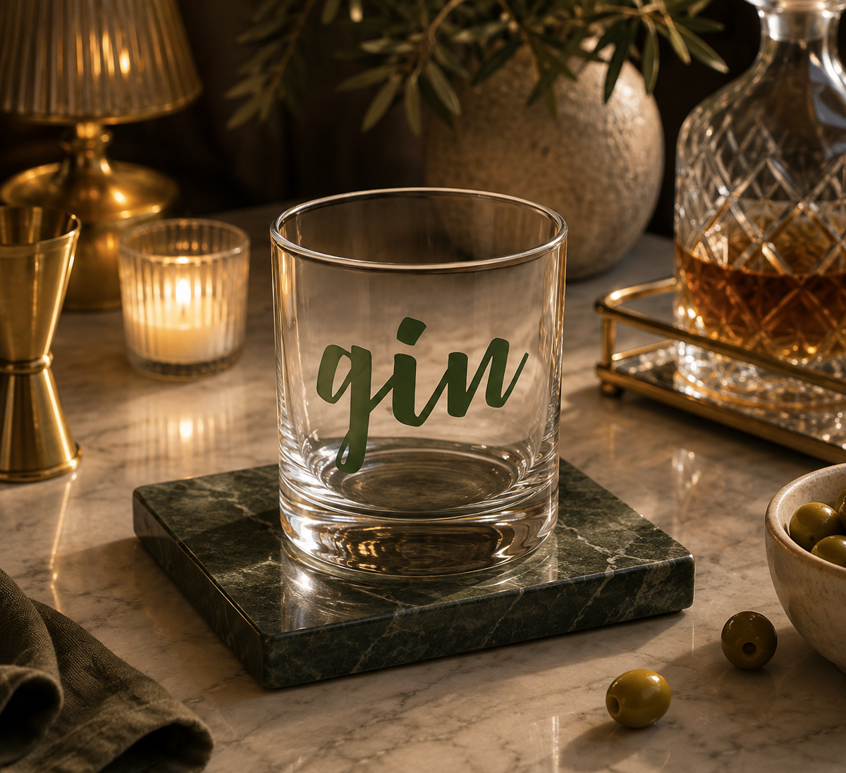 A clear lowball-style glass with the word "gin" in dark green script