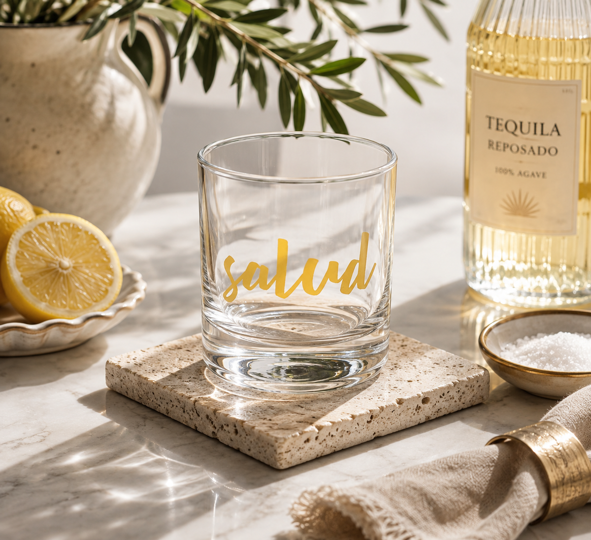 A clear rocks glass with the word 'salud' in gold script