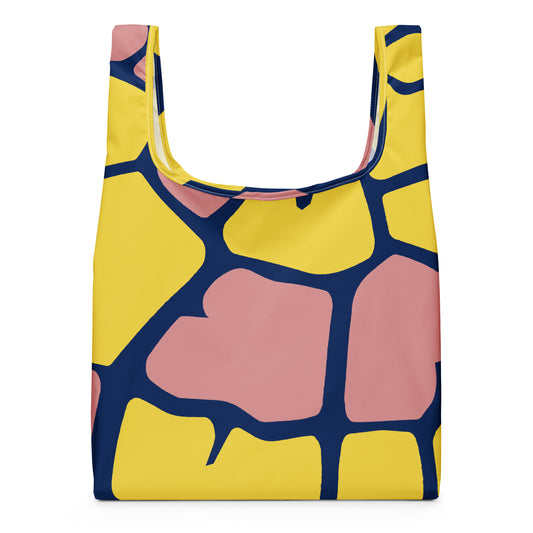 A reusable tote bag with a bold abstract geometric pattern featuring yellow, dusty pink, and navy blue shapes. 