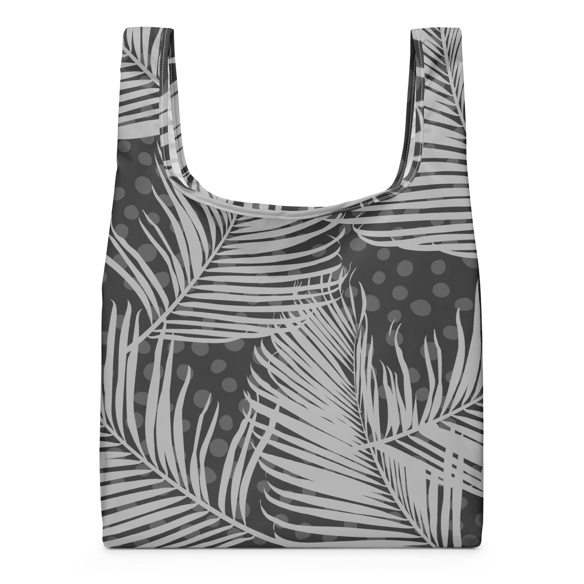 A reusable tote bag with a gray and white tropical palm leaf pattern and dark gray polka dots.