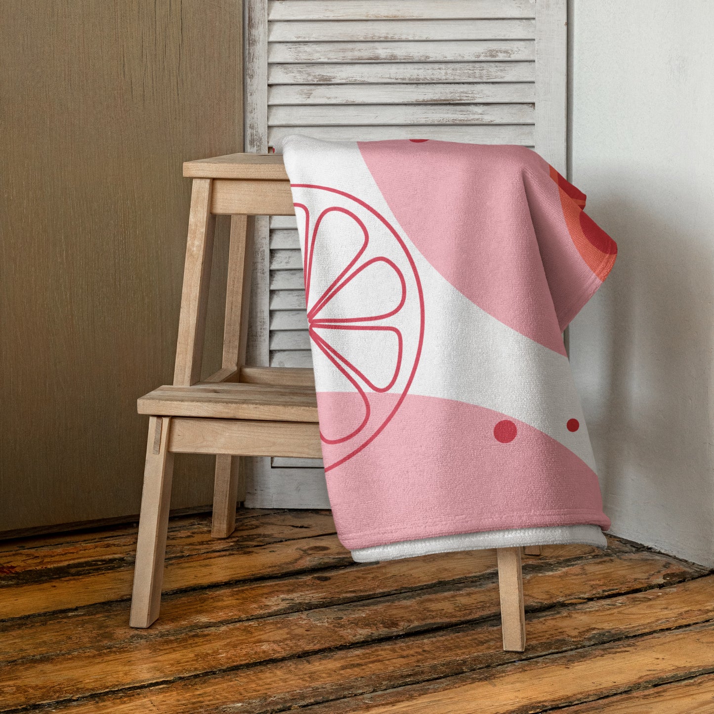 A pink and white beach towel with a red citrus slice graphic.