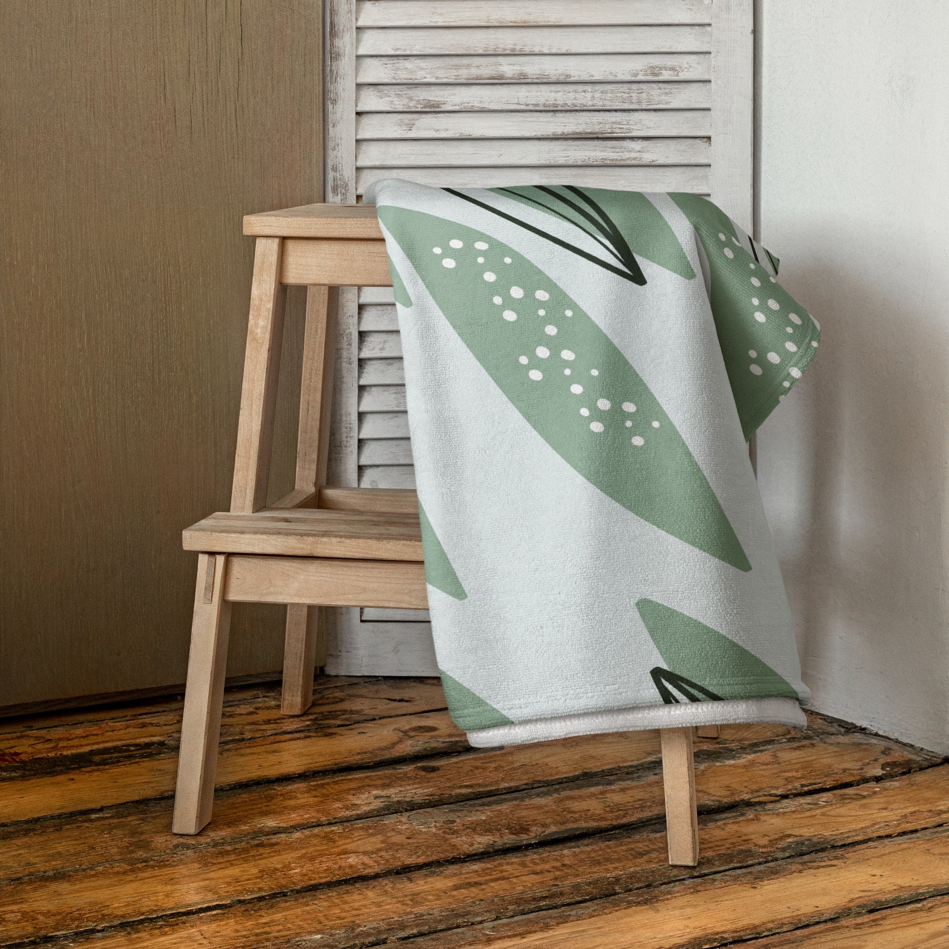 A light gray beach towel with a green and white botanical leaf pattern.