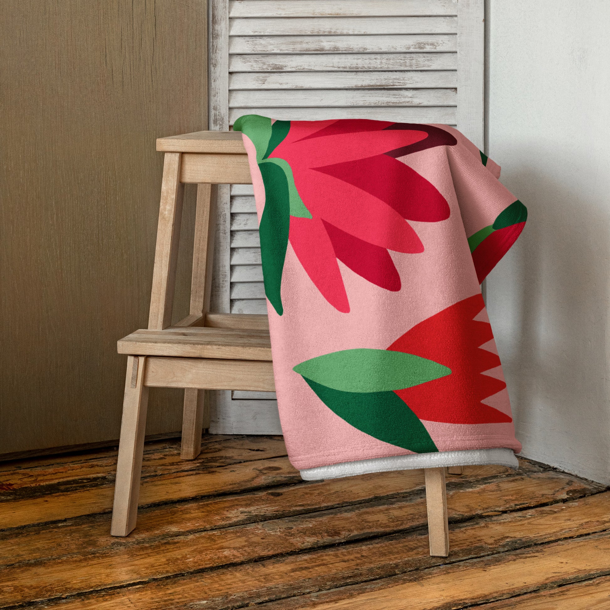 A pink beach towel with a bold red and green floral pattern.