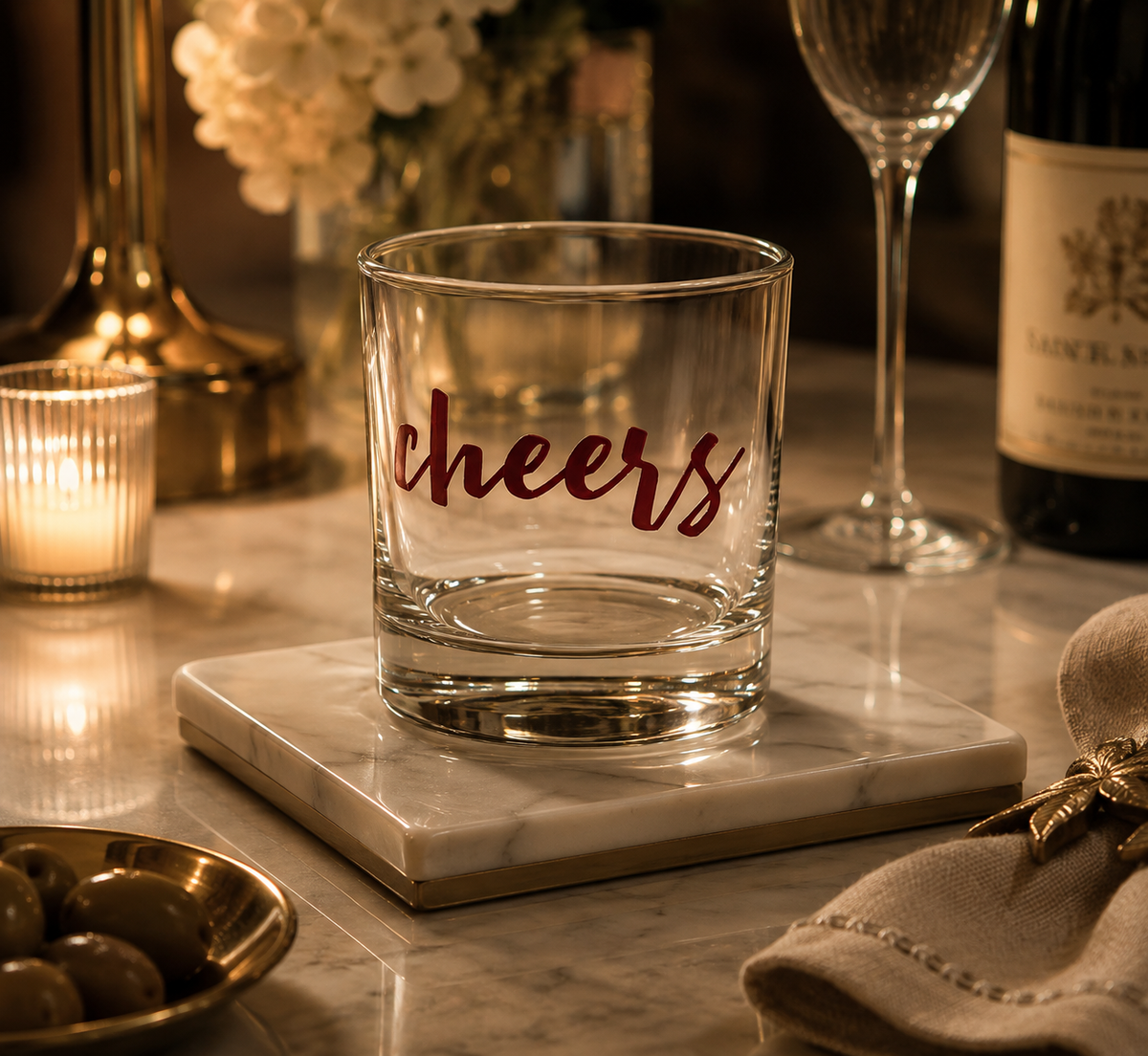 A clear glass rocks tumbler with the word 'cheers' in dark red script