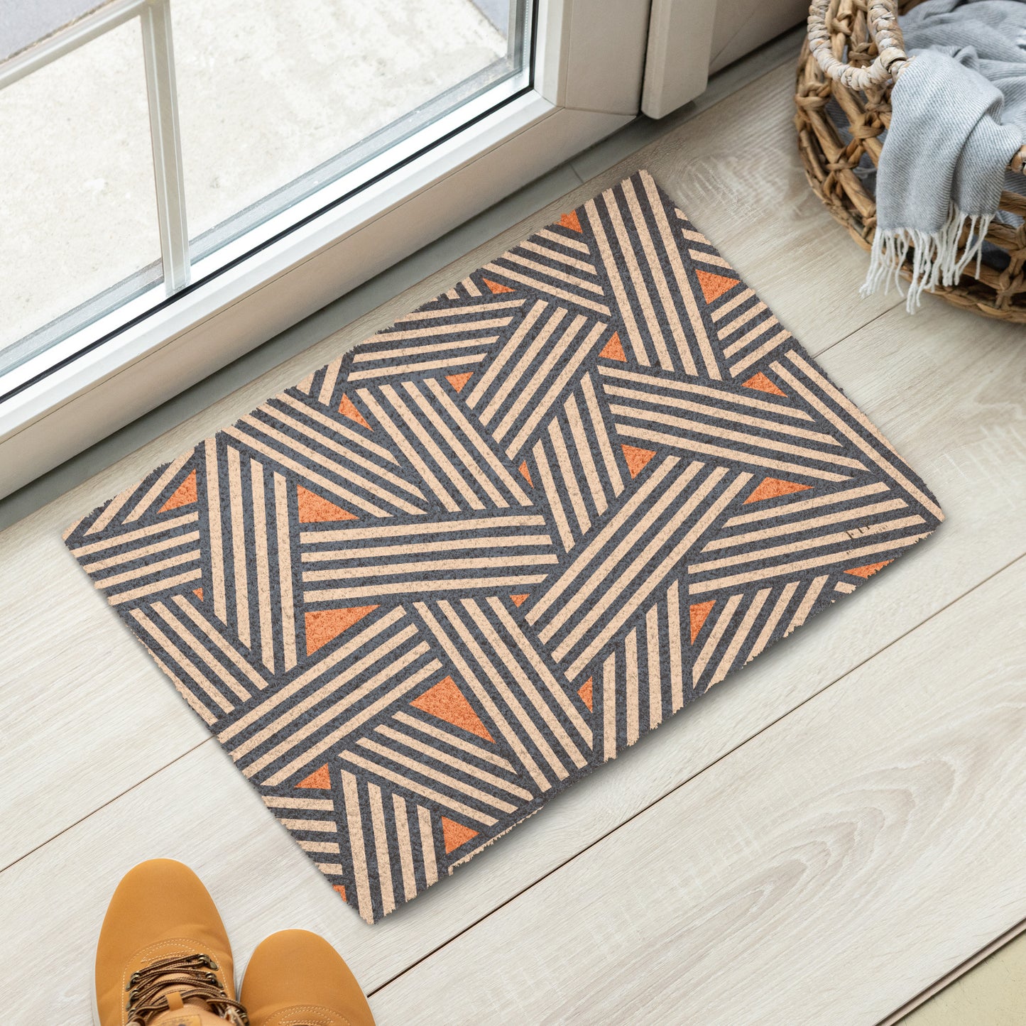 A rectangular doormat with a geometric pattern of beige and dark gray stripes and orange triangles.