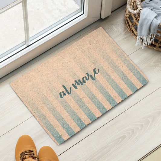 A rectangular coir doormat with vertical beige and muted teal stripes and the script text 'at mare' in dark teal. 