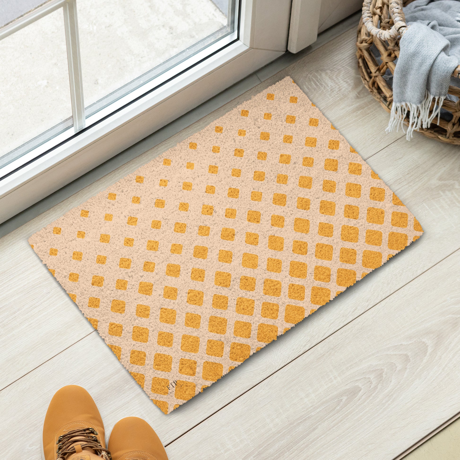 A rectangular doormat with a repeating yellow-orange geometric pattern on a light beige background