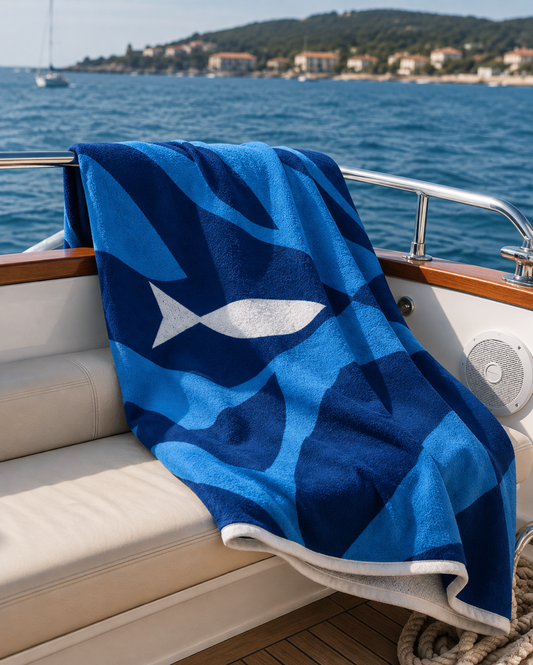 A blue and navy patterned beach towel with a white fish design 
