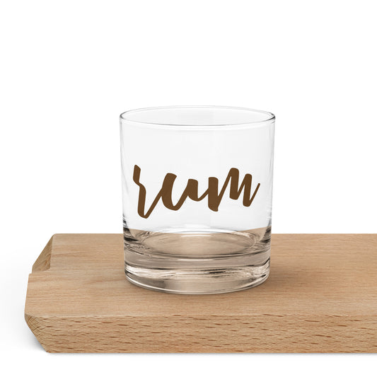 A clear glass rocks tumbler with the word 'rum' printed in brown script.