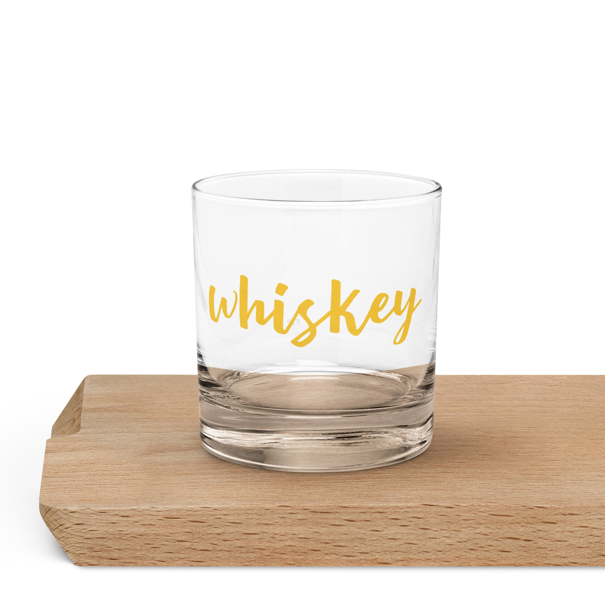 A clear glass rocks tumbler with the word 'whiskey' printed in yellow script. 