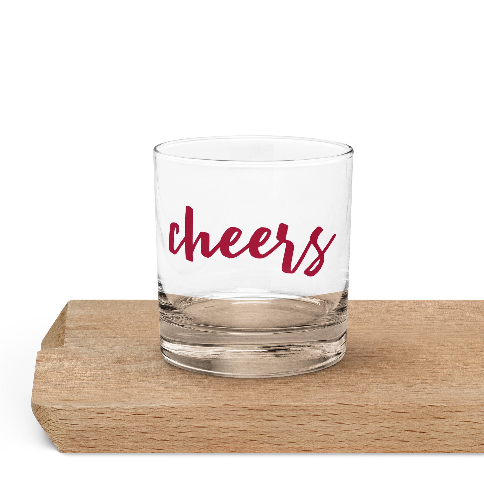 A clear glass rocks tumbler with the word 'cheers' printed in red script.