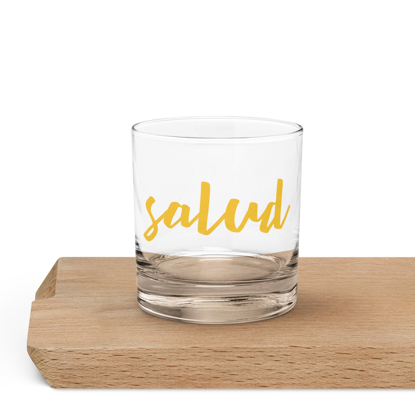 A clear rocks glass with the word 'salud' printed in yellow script.