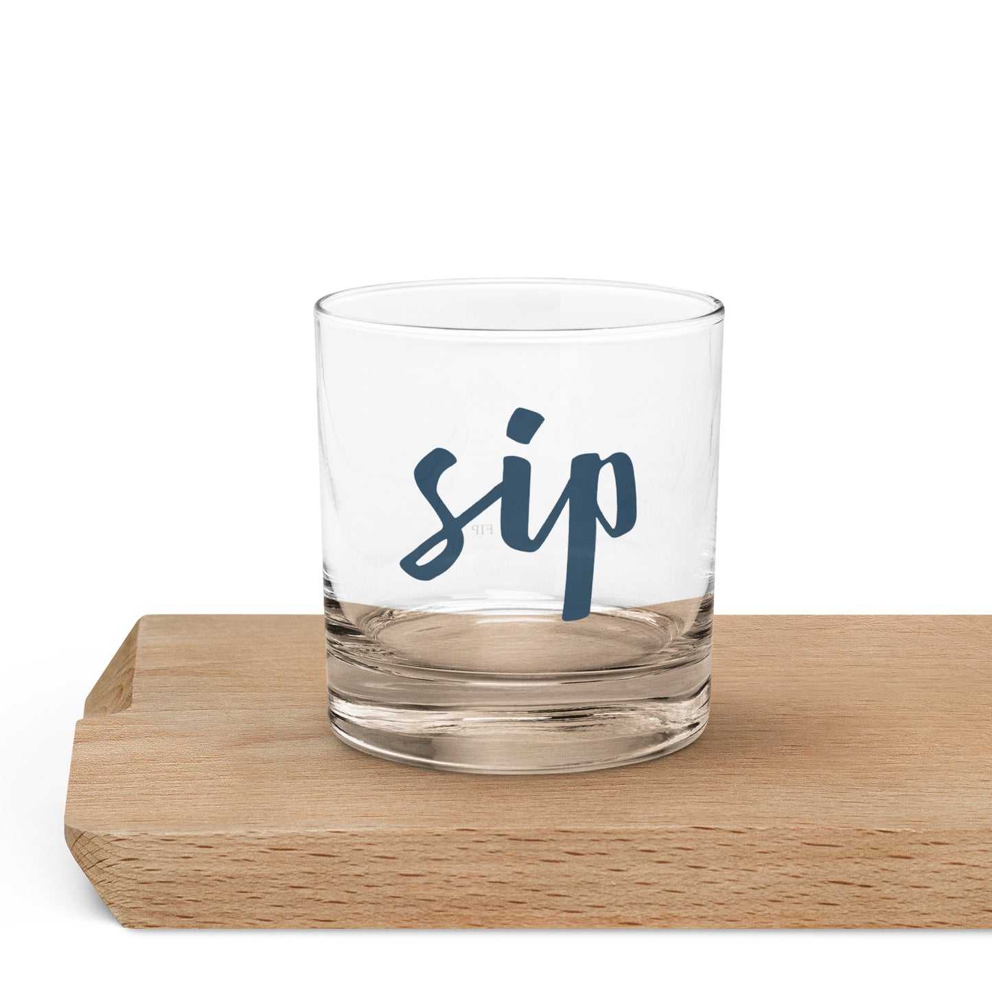 A clear glass rocks tumbler with the word 'sip' printed in dark blue script. 