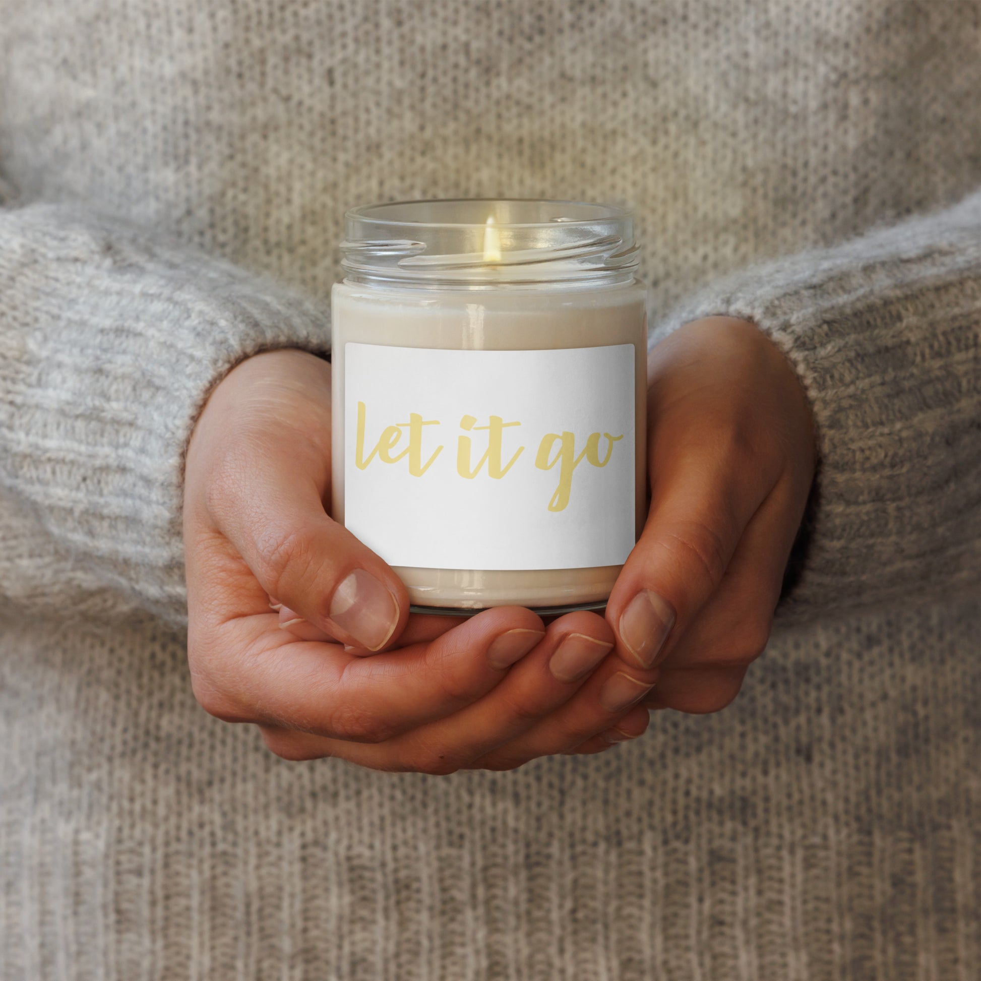 soy scented glass jar candle with a white label that reads 'let it go' in gold script.