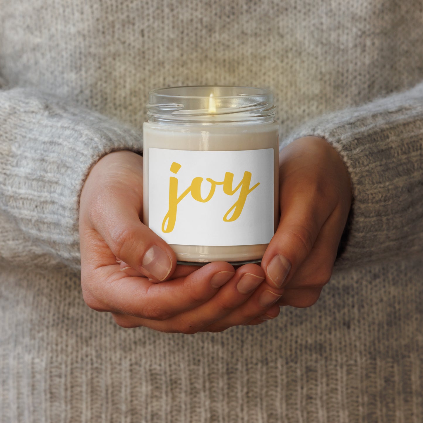 a clear glass jar with a white label reading 'joy' in gold script scented soy candle