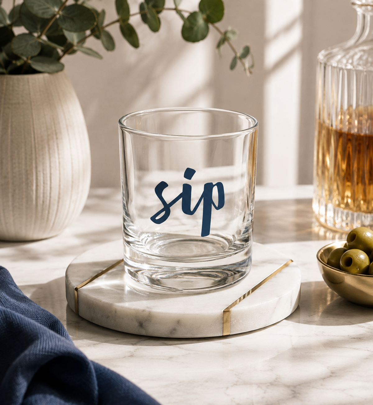 A clear rocks glass with the word 'sip' printed in navy script