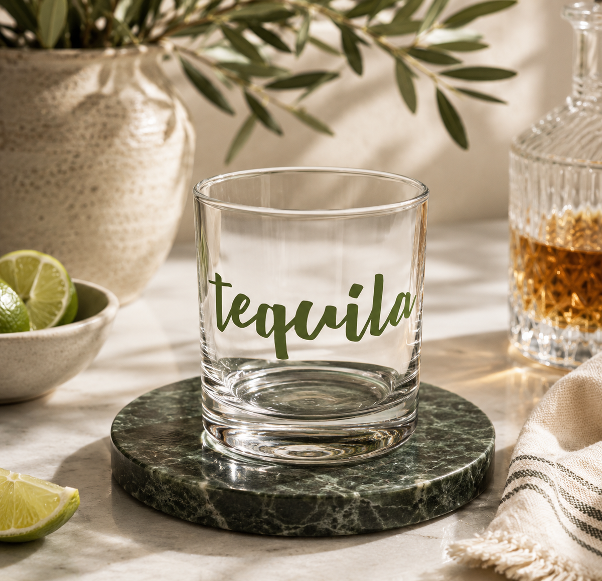 A clear glass rocks tumbler with the word 'tequila' in green script
