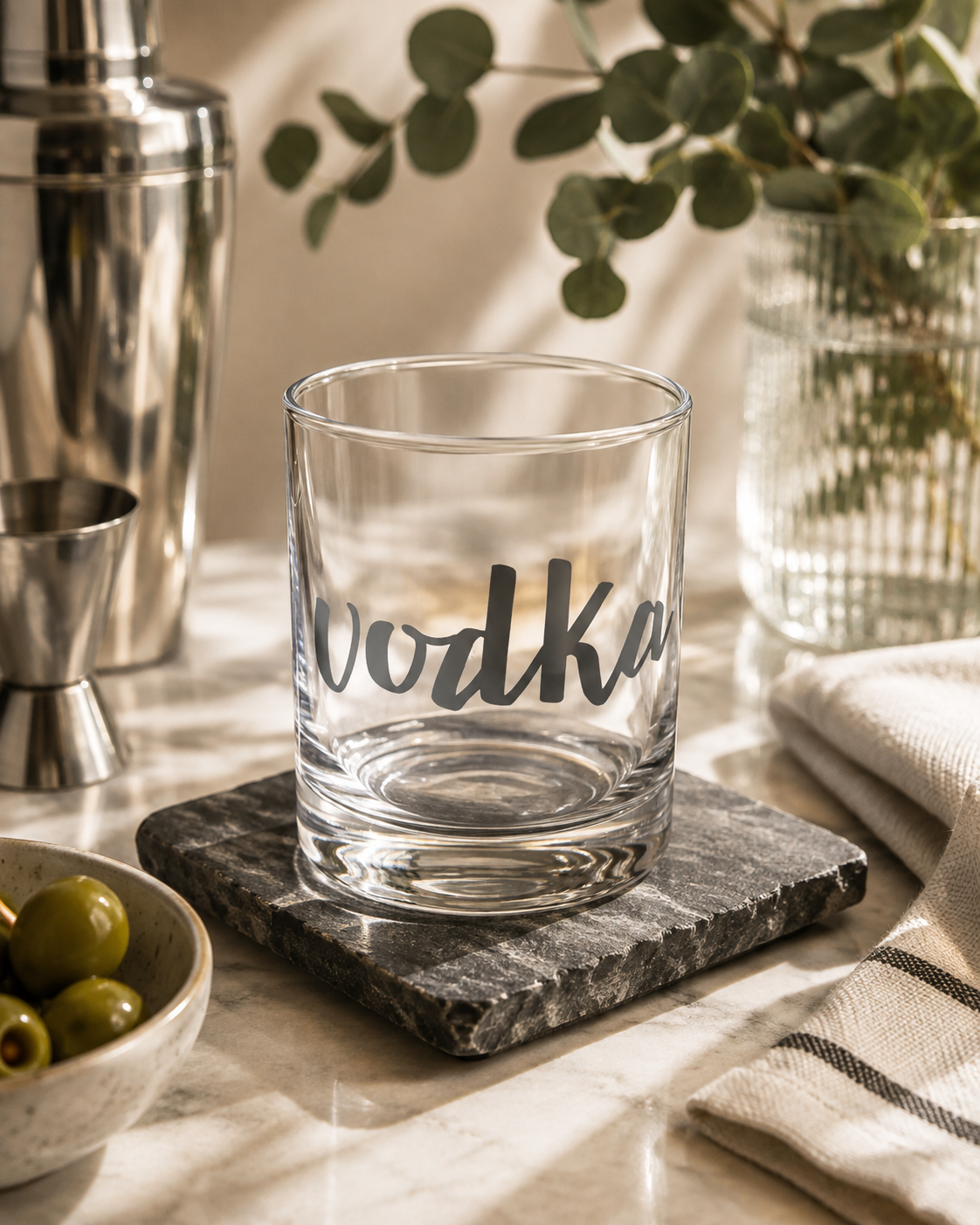 A clear glass rocks tumbler with the word 'vodka' printed in grey script