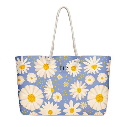A light blue tote bag with a white and yellow daisy floral pattern, featuring two white rope handles. 