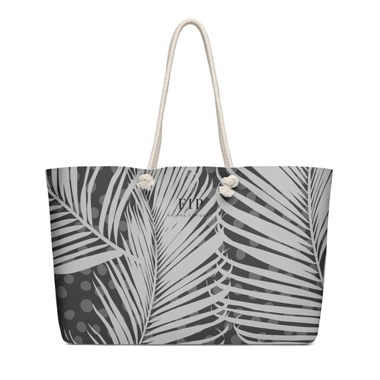 A tote bag featuring a black and white palm leaf pattern, with cream-colored rope handles. 