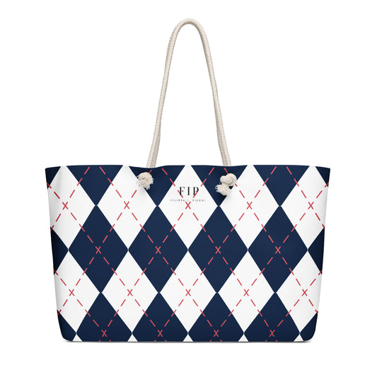A tote bag with a navy blue and white argyle pattern, accented with thin red dashed lines and featuring off-white rope handles.