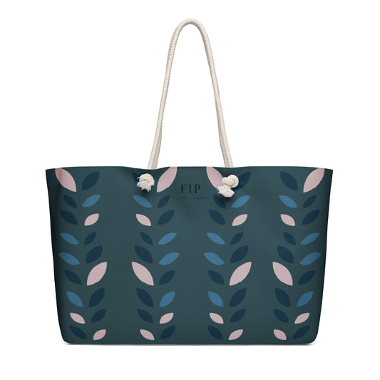 A dark teal tote bag with a vertical pattern of blue and pink leaves, featuring cream rope handles 