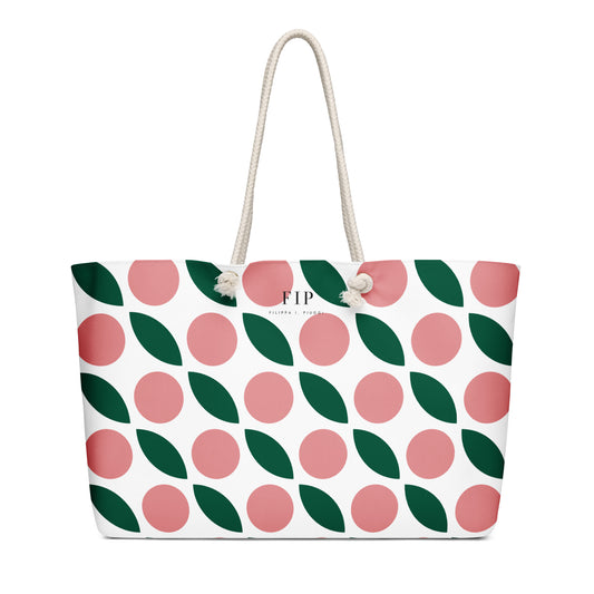 A white tote bag with a repeating pattern of pink circles and dark green leaves, featuring off-white rope handles 