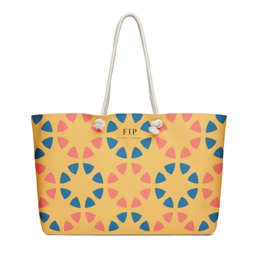 A yellow tote bag with a geometric pattern of blue and pink triangles, featuring white rope handles.